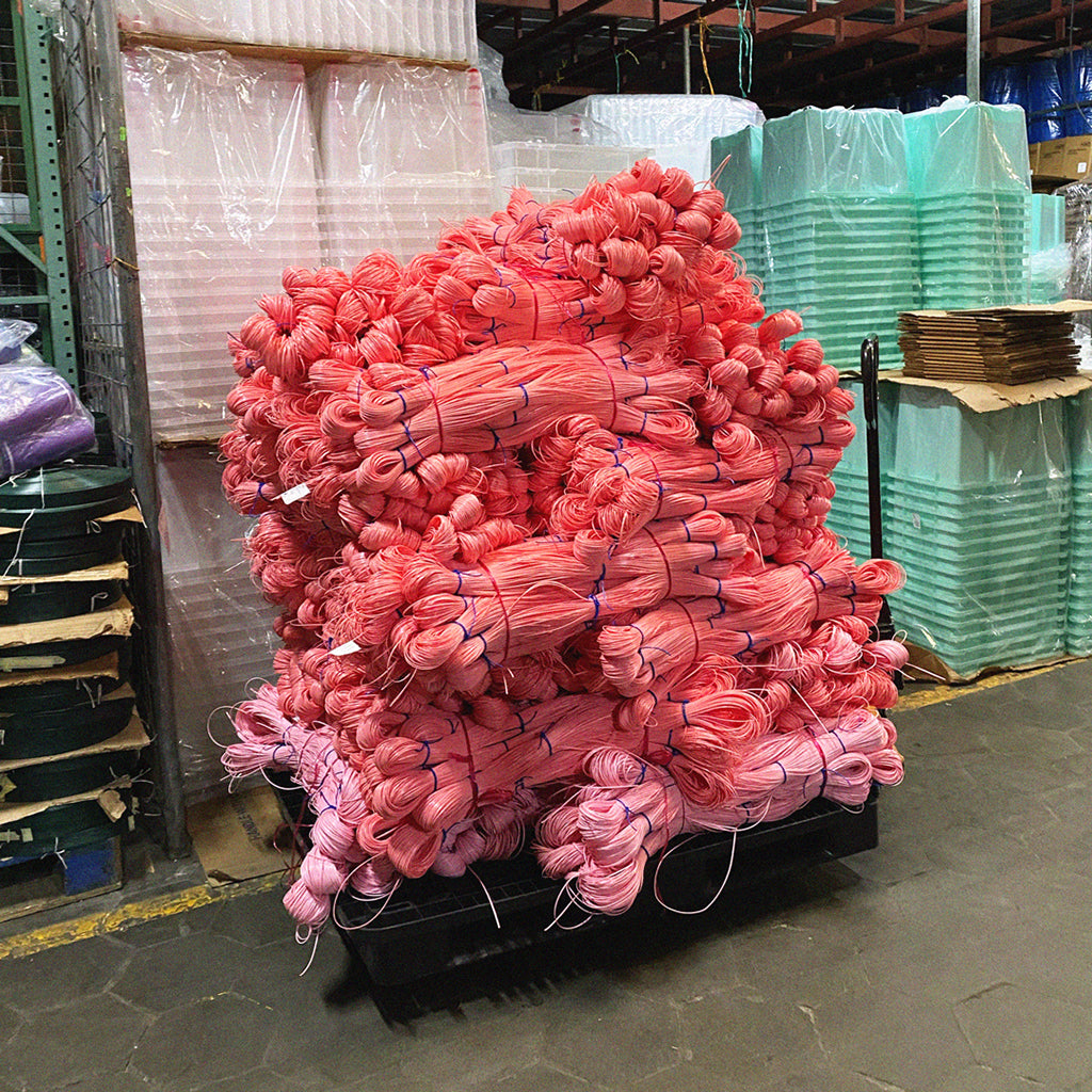 A pile of pink plastic strips that are used for weaving colourful baskets